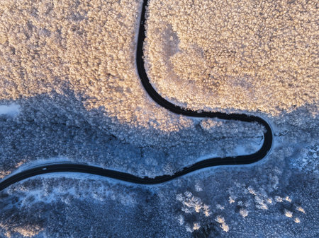 Aerial view of winter landscape with snow covered mountain hills and winding forest road in morningの写真素材