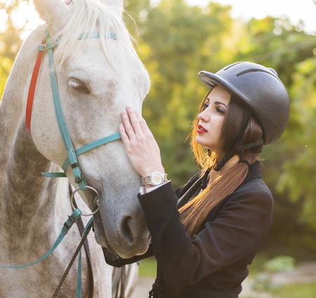 Young brunette beauty girl gently caressing her horse in the parkの写真素材