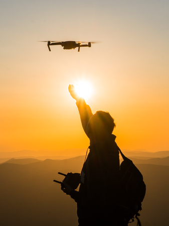 Silhouette of young man catching drone at sunset for photos and video making - Happy man having fun with new technology trends in mountainsの写真素材
