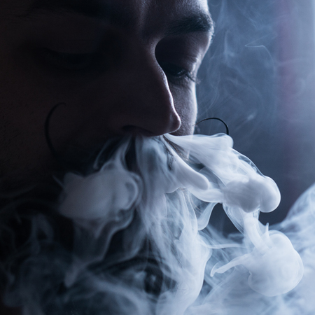 Young Man with Beard and Mustages Vaping an Electronic Cigarette. Vaper Hipster Smoke Vaporizer and Exhals Smoke Flow from Nose.の写真素材