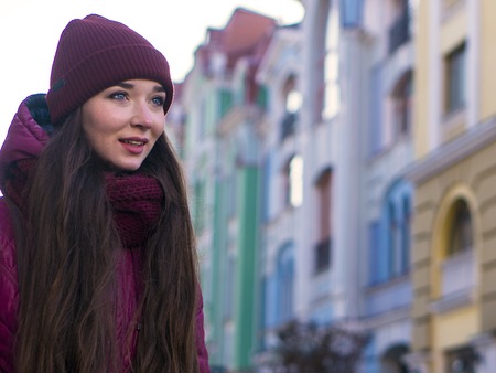 Pretty Smiling Brunette Girl Wearing Purple Winter Coat, Hat and Scarf, Walking by European Street at Winterの写真素材