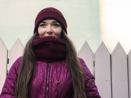 Pretty Brunette Girl Wearing Purple Winter Coat, Hat and Scarf, Walking by European Street at Winter, Wrapped up in a Scarf.の写真素材