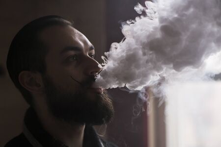 Man with Beard and Mustages Vaping an Electronic Cigarette. Vaper Hipster Smoke Vaporizer and Exhals...