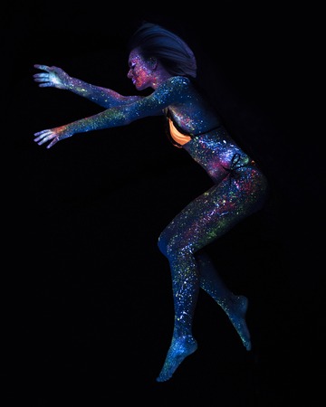 Portrait of Beautiful Fashion Woman Flying in Neon UF Light. Model Girl with Fluorescent Creative Psychedelic MakeUp, Art Design of Female Disco Dancer Model in UVの写真素材