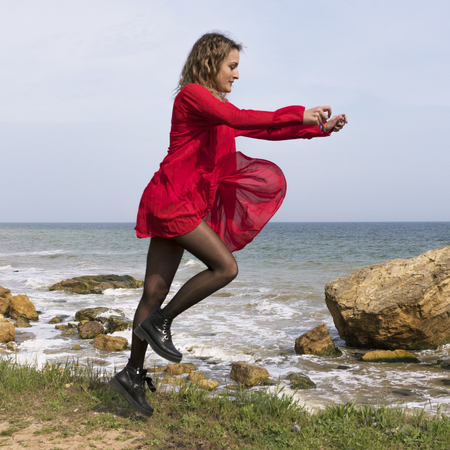 Happy Young Woman in Red Dress Have Fun at the Sea Coast Cliffの写真素材