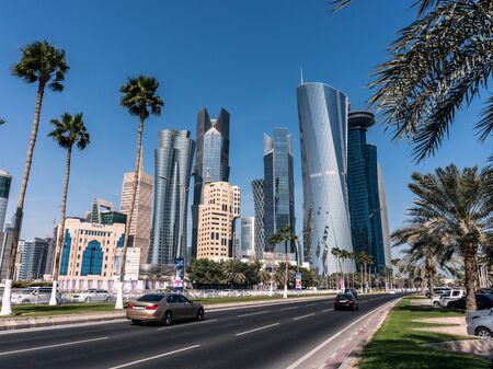 DOHA, QATAR - FEB 2018: Road with Palm Trees Head to Modern Blue High Skyscrapers in Doha city, qatarのeditorial素材