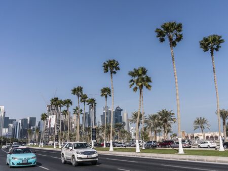 DOHA, QATAR - FEB 2018: Road with Palm Trees Head to Modern Blue High Skyscrapers in Doha city, qatarのeditorial素材