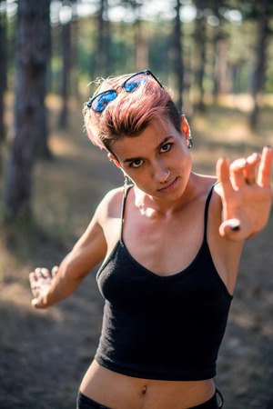Young Pretty Punk Girl in Collar and Black Cloth with Pink Hair in Pine Forest at Sunset Timeの写真素材