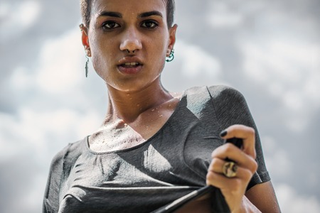 Expressive Pierced Girl in Wet t-shirt with Cloudy desaturated sky on background.の写真素材