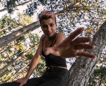 Girl Held out her hand. Young Punk Girl in Black Top with Pink Hair in Pine Forestの写真素材