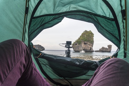 Lifestyle image with legs in purple jeans on foreground of POV view from a tent on the beach of the...