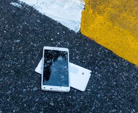 Broken New Smartphone on asphalt road. Someone dropped device. Cracks on a big displayの写真素材