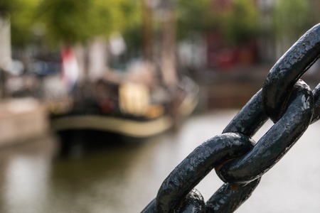 Black maritime Chain Close Up. Traditional wooden sailing ship with flag and sign on a board in channel blured on background. Old historic harbor of Schiedam, The Netherlandsの写真素材