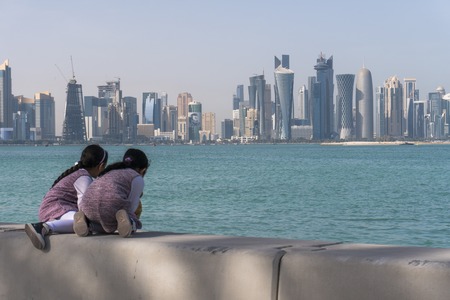 Two Arabian Middle Easter Little Child Girls Sitting on Corniche Broadway and Looking on the Doha Skyline View. Qatar, Middle Eastの写真素材