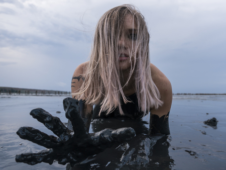 Stretched hand of Blonde Caucasian Girl Crawls Smeared in a Healthy Black Mud in old Firth