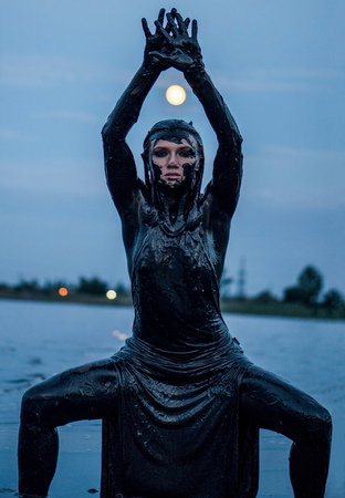 Slender Caucasian Girl Stays Smeared in a Healthy Black Mud in old Firth. Legs set wide apart and moon above her Headの写真素材