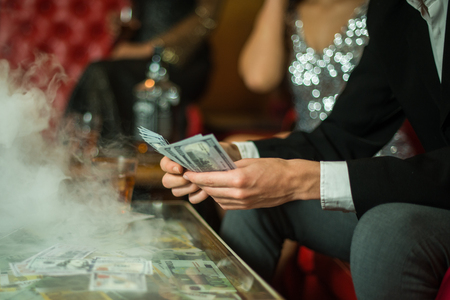 Man with cigar counting money in the club. Group of young multi-ethnic friends relaxing in shisha club-bar in rich interiorの写真素材