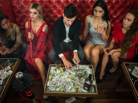 Group of young multi-ethnic friends relaxing in shisha club-bar in rich interior. Man with cigar counting money in the clubの写真素材