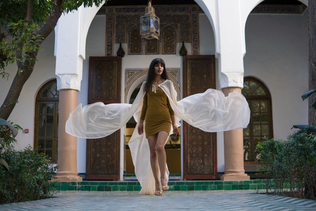 Beautiful Moroccan Girl walking and Waving her white mantle in Rich interior of Picturesque Dar Si...