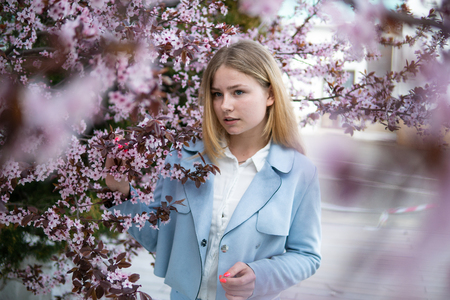 Portrait of Beautiful blonde girl posing in blooming tree branches with pink flowers. Spring seasonの写真素材