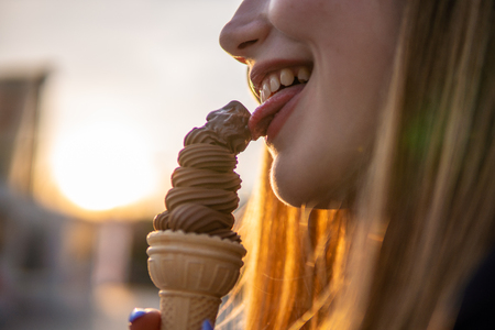 Mouth of young girl licking brown ice cream at evening sunset lightの写真素材