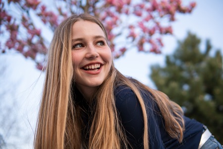 Portrait of Beautiful blonde girl posing with blooming Magnolia tree branches with pink flowers on...