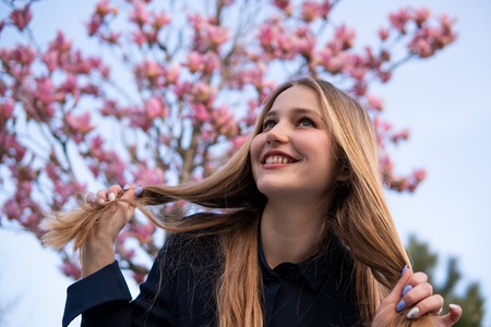 Portrait of Beautiful blonde girl posing with blooming Magnolia tree branches with pink flowers on...
