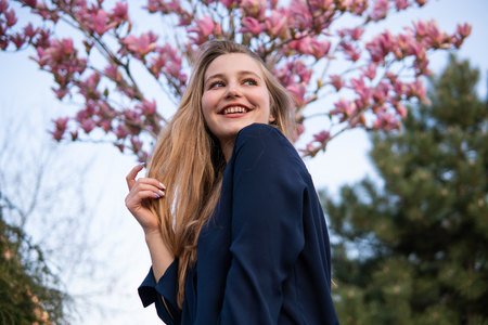 Portrait of Beautiful blonde girl posing with blooming Magnolia tree branches with pink flowers on background. Spring seasonの写真素材