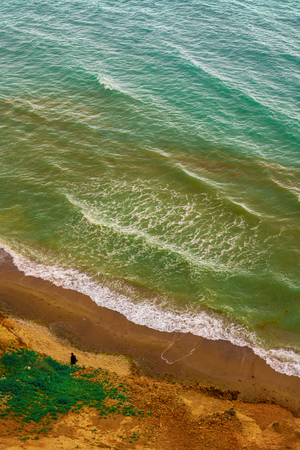 Aerial view at young woman walking far away by the colorful sea shoreの写真素材