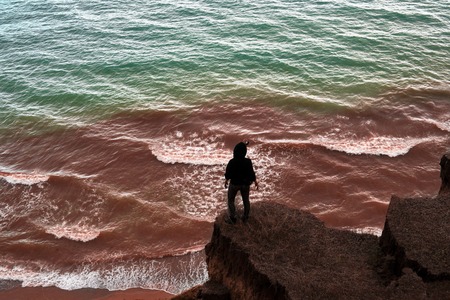 Young woman standing on the top of the rock and looking at the sea