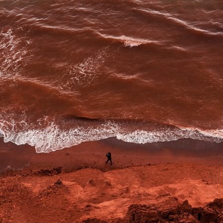Aerial view at young woman walking far away by the brown unkind water sea shore
