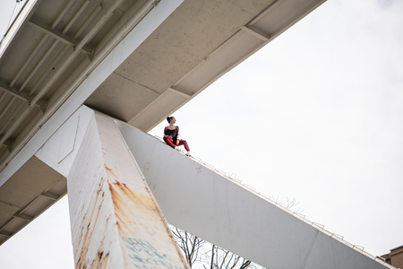 Young extremal fearless woman climb up under the bridge and having fun. Dangerous tricks and risking without insurance ropeの写真素材