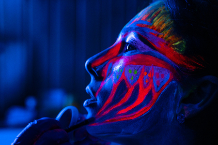 Ultraviolet black light glowing bodyart processing on young womans face. Pink and purple dyes in...