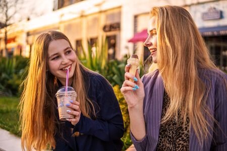 Two girls friends having fun on evening Broadway. Eating ice cream, drinking ice fresh milk shake