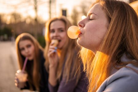 Three girls friends having fun on evening roadway. Eating ice cream, drinking ice fresh milk shake...