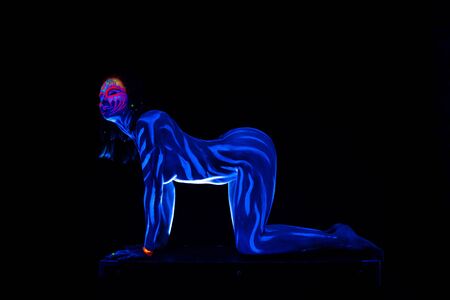 Young naked bodyarted woman in blue glowing ultraviolet paint moving and teasing. Sexy nude girl dancingの写真素材