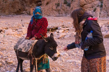 ATLAS MOUNTAINS, MOROCCO - 20 JAN: Tourist girl and Nomad tribe people living in mountains near Tinghir or Tinerhir. Woman with her daughters are herding donkeys in canyon near the river. Todra gorgeのeditorial素材