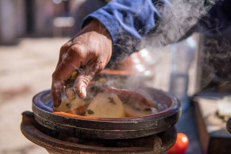 A hand of man cooking traditional Tajine in steam vapor on an outdoor barbecue at town square on the street in Morrocoの写真素材