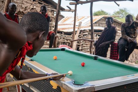 TANZANIA, NATRON LAKE - JANUARY 2020: African masai men playing open air billiard pool in the village Sengare Sero at Maasailandのeditorial素材
