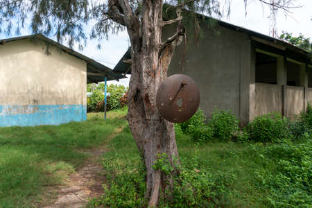 Rusty School Bell For Signalize about a School Brake Hanging on the Tree Near African school building in Primary School Yard in remote Africa Villageの写真素材