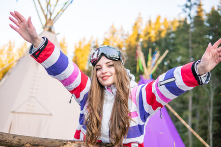 Portrait of Cheerful Pretty Caucasian young woman Near Tipi or Wigwam in ski outfit and Winter Sports Mask on her Head. Blond woman at ski resortの写真素材