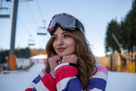 Portrait of Happy Pretty Caucasian woman in ski outfit and With Snowboarding Mask on her Head. Portrait of cheerful blond woman at ski resortの写真素材