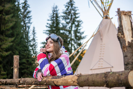 Portrait of Pretty Caucasian young woman Near The Indian Tipi or Wigwam in ski outfit and Winter Sports Mask on her Head. Portrait of cheerful blond woman at ski resortの写真素材