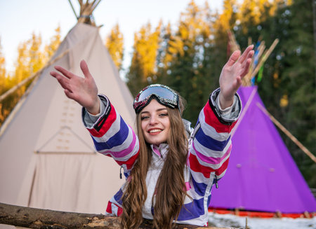 Portrait of Pretty Caucasian young woman Near The Indian Tipi or Wigwam in ski outfit and Winter Sports Mask on her Head. Portrait of cheerful blond woman at ski resortの写真素材