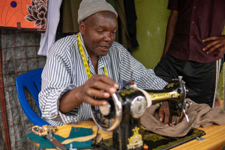 TANZANIA, MASAI VILLAGE - JANUARY 2020: Portrait of Sewer of Swiss Tailor Maasai man working With sewing machine in native masai village in Maasailand, Arusha districtのeditorial素材