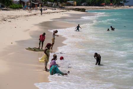Nungwi, Zanzibar - December 2019: Boys and Girls in Turquoise Water. African children playing on the beach Ocean Surf Waves at Sunny Day at Nungwi village in northern Zanzibar, Tanzaniaのeditorial素材