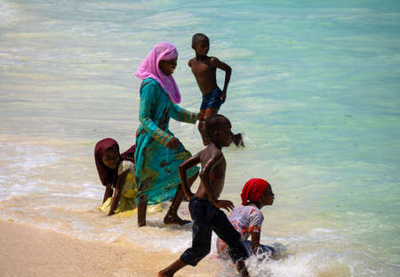 Nungwi, Zanzibar - December 2019: Boys and Girls in Turquoise Water. African children playing on the beach Ocean Surf Waves at Sunny Day at Nungwi village in northern Zanzibar, Tanzaniaのeditorial素材