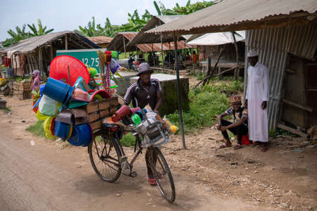 Zanzibar, Tanzania - JANUARY 2020: Black African Man with Bicycle Loaded with Good and Household Tools on Village Streets of Zanzibarのeditorial素材