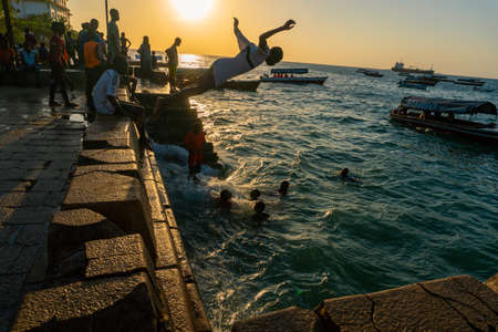 Stone Town, Zanzibar, Tanzania - January 2020: Locals run and jump into the sea From Stone Embarkment at Sunset timeのeditorial素材