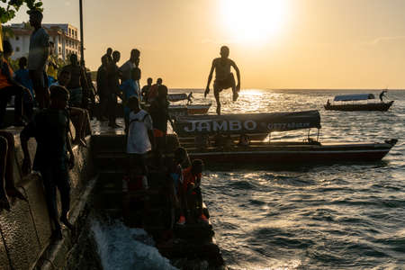 Stone Town, Zanzibar, Tanzania - January 2020: Locals run and jump into the sea From Stone Embarkment at Sunset timeのeditorial素材